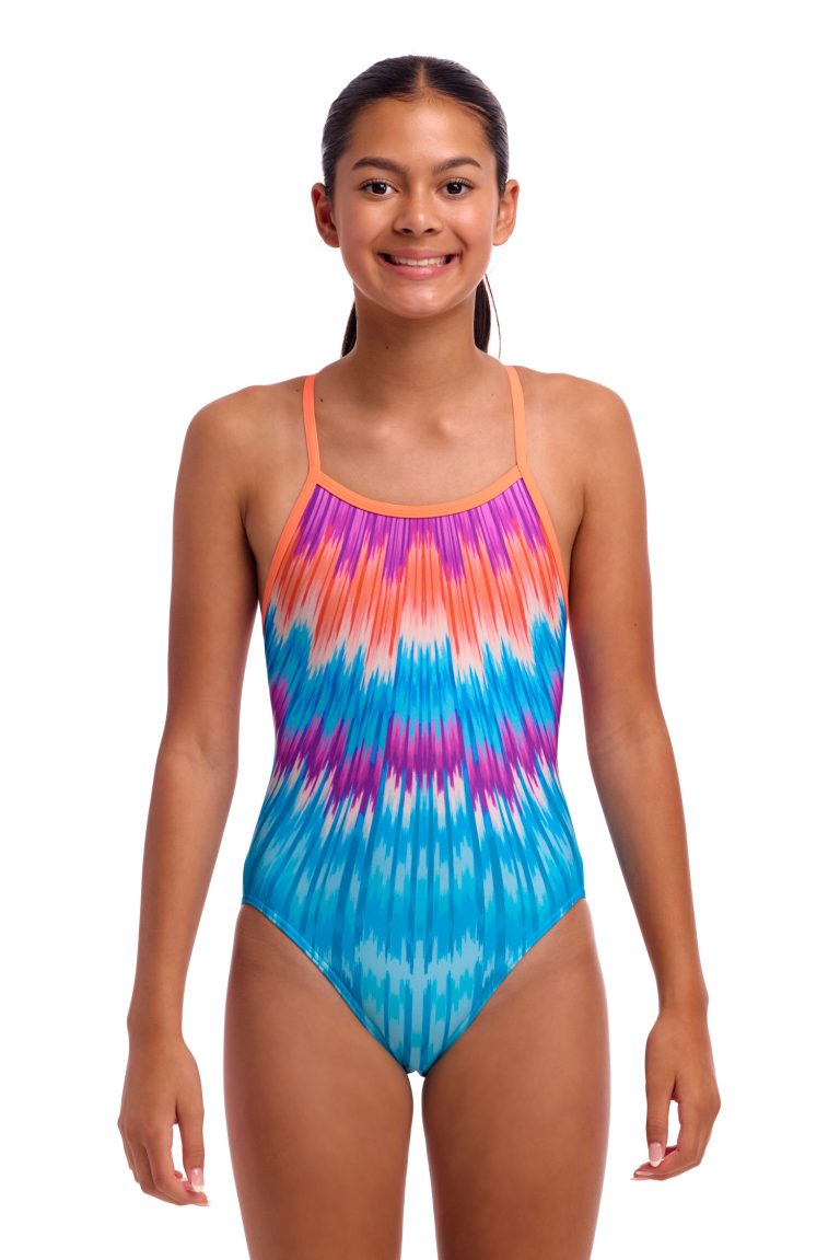 En ung kvinde smiler og ser fremad mod en hvid baggrund, mens hun er iført Funkita Birdie Bird - Single Strap - Piger badedragt i ét stykke med et farverigt batikmønster i orange, lilla og blå.