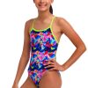 En smilende pige med langt mørkt hår i hestehale bærer Funkita Birdie Bird Single Strap badedragt i ét stykke med et farverigt abstrakt mønster og grønne stropper. Hun står på en hvid baggrund med den ene hånd på hoften.