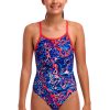 En ung person står og smiler iført Funkita Mad Cat - Diamond Back one-piece badedragt i et abstrakt blåt, rødt og hvidt mønster med røde stropper på en almindelig hvid baggrund.