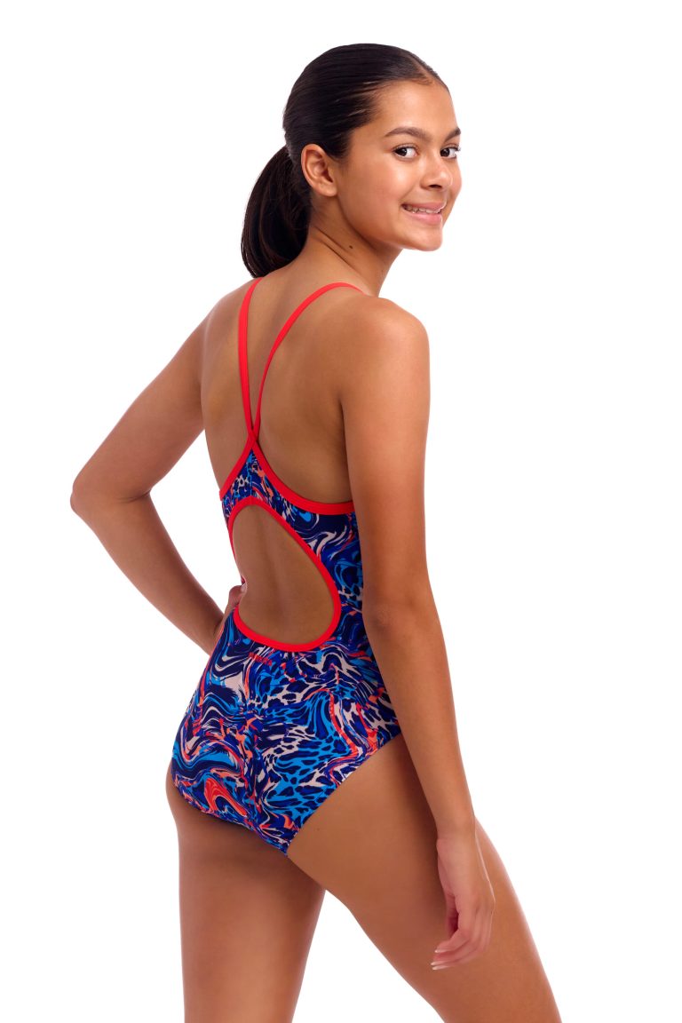 En kvinde med mørkt hår, der er bundet tilbage, smiler og viser bagsiden af sin Funkita Mad Cat - Diamond Back - Piger-badedragt med røde stropper og et farverigt, hvirvlende blåt, rødt og hvidt design på en almindelig hvid baggrund.