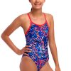 En ung pige smiler i badedragten Funkita Mad Cat - Diamond Back - Piger, der har et levende blåt, rødt og hvidt mønster med røde stropper. Hendes hår er trukket tilbage, mens hun poserer selvsikkert mod en hvid baggrund.