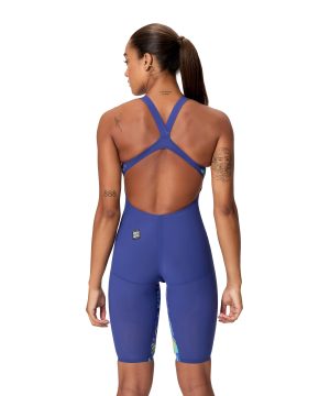 En kvinde med hestehale og tatoveringer på arme og skuldre står med ryggen til kameraet i en Speedo Fastskin LZR Pure Valor 2.0 Open Back Kneeskin (Navy/Multi) badedragt. Baggrunden er hvid.